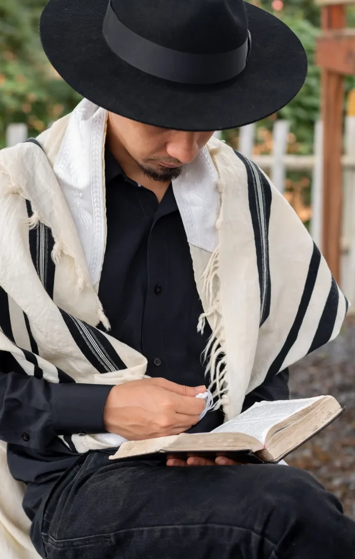 Latin Jew wearing tallit and Jewish hat sitting reading scripture in the quiet of his courtyard.